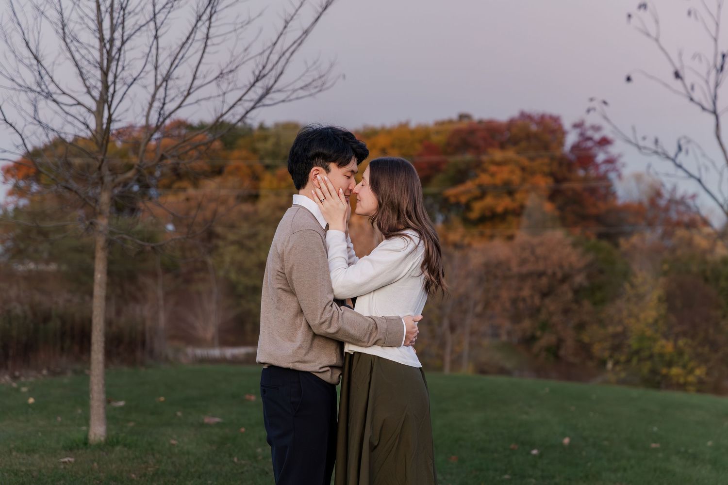 A couple shares a romantic moment surrounded by vibrant red fall foliage in an autumn park setting.