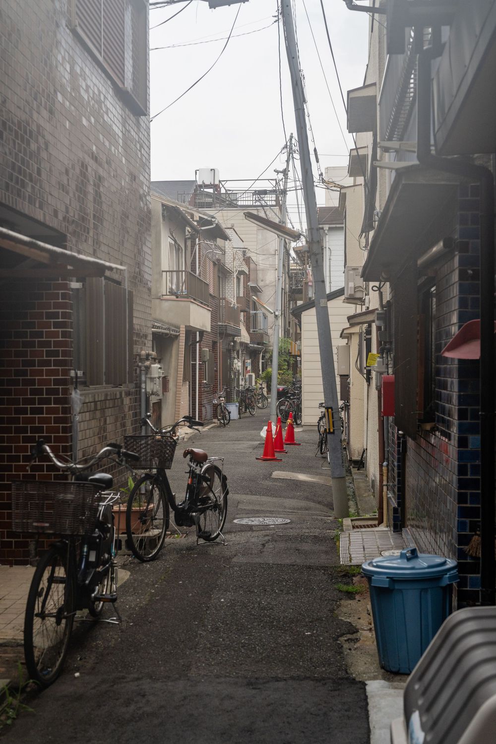 Urban back street in Japan with bicycles and red traffic cones.