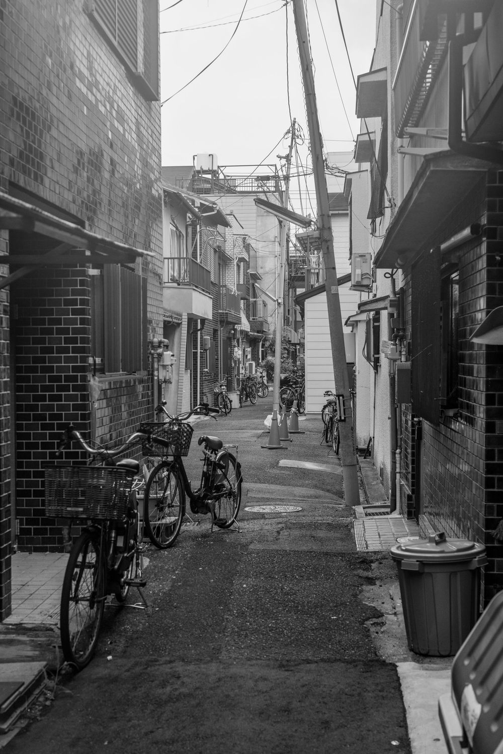 Narrow alleyway in Japan with parked bicycles and brick buildings on both sides.
