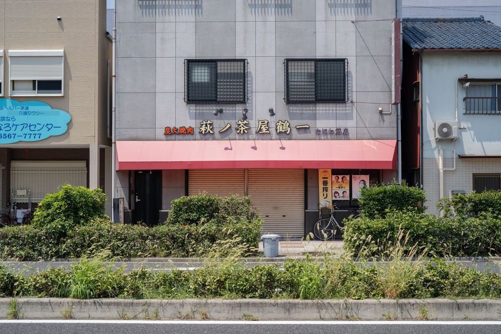 Row of modern Japanese buildings with greenery and fencing.