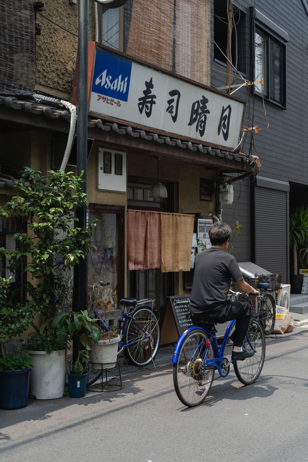 Bicycles parked outside traditional Japanese shops with Asahi beer signs and kanji characters.