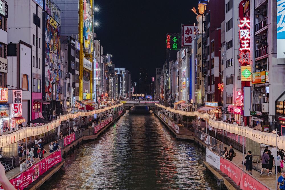 Dotonbori Canal at night with neon lights reflecting on the water between urban buildings.