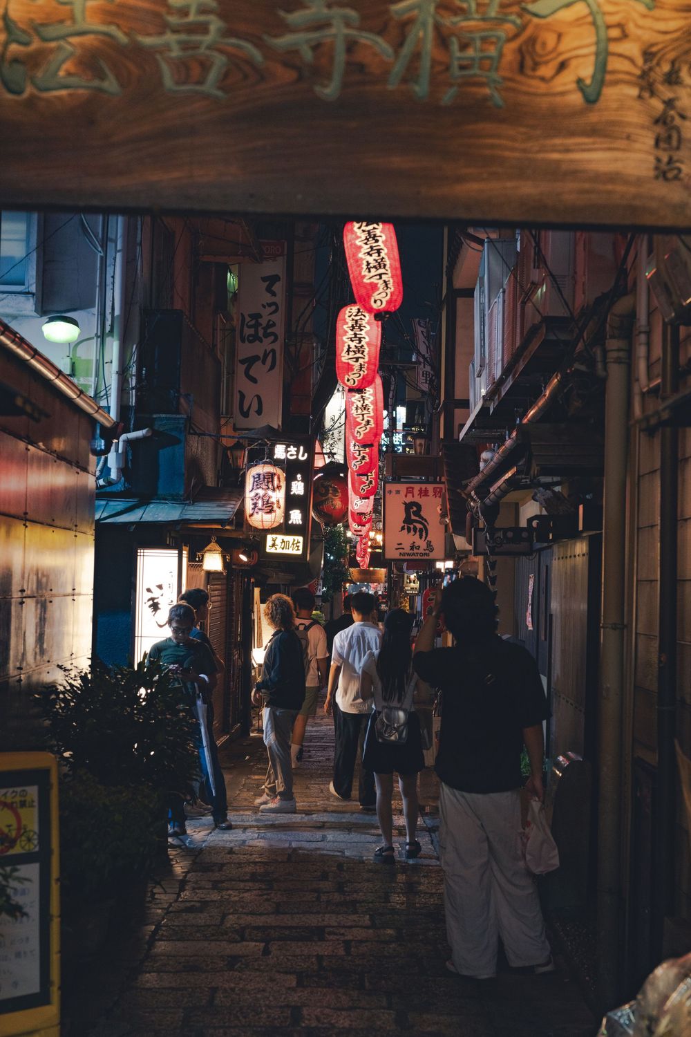 Atmospheric nighttime alley in Japan with glowing red lanterns and traditional wooden architecture.