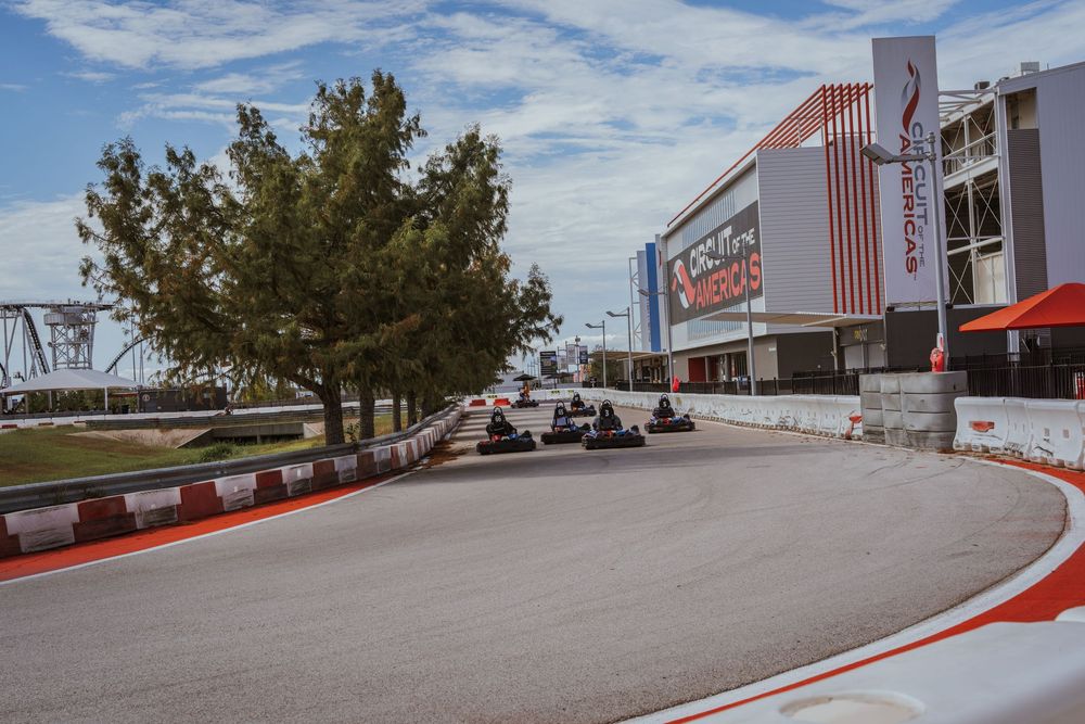 Aerial view of go kart racing track with red and white barriers under blue sky.