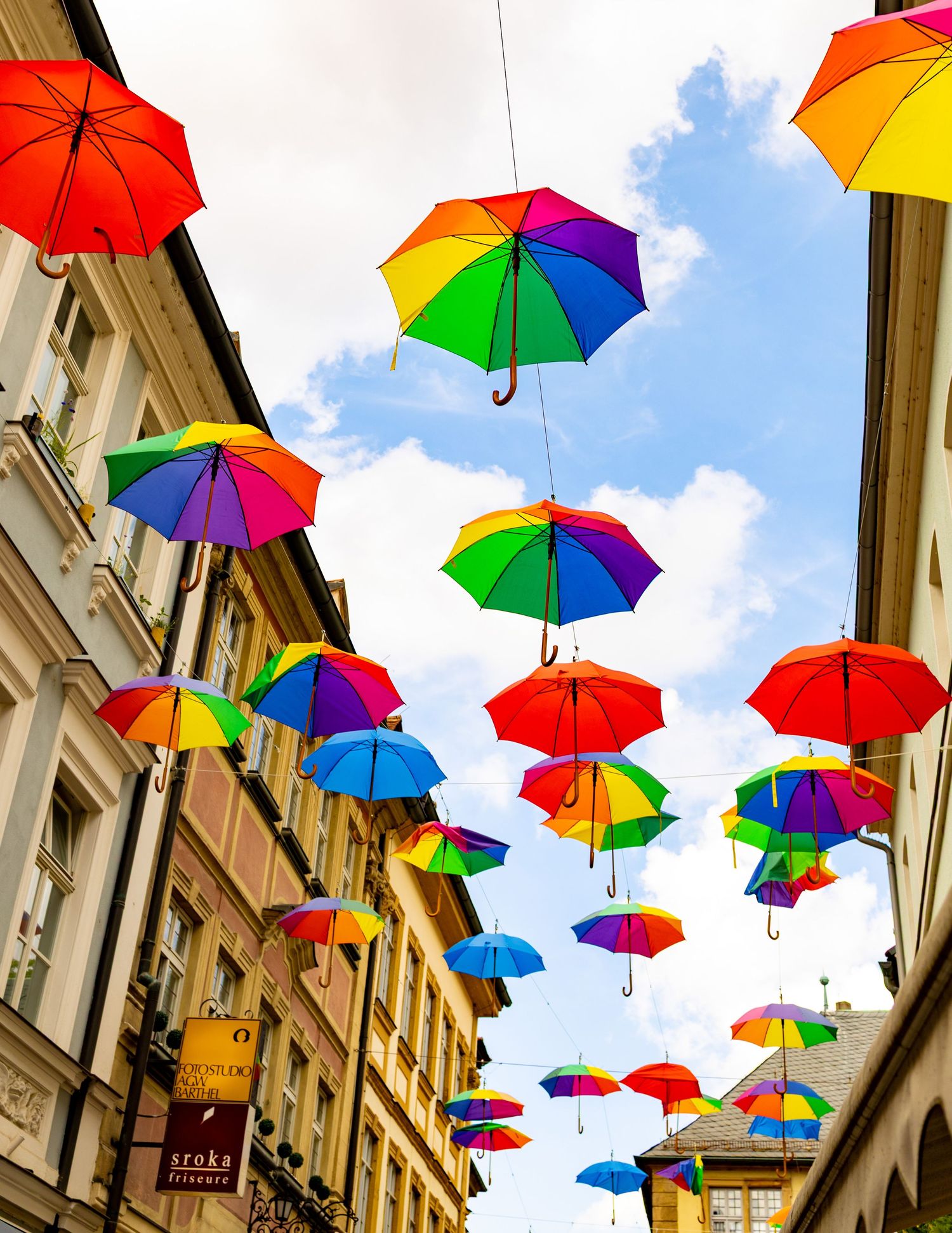 Colorful rainbow umbrellas hanging above a charming European street creating a festive canopy.