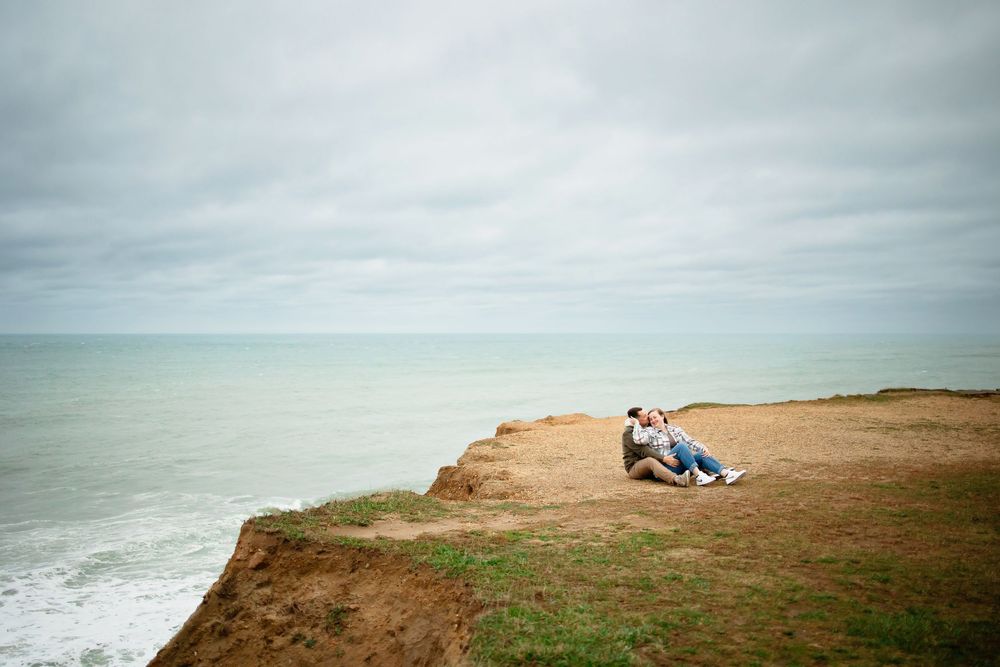 Scenic coastal cliffs overlooking the Pacific Ocean with dramatic cloudy skies and grassy terrain.