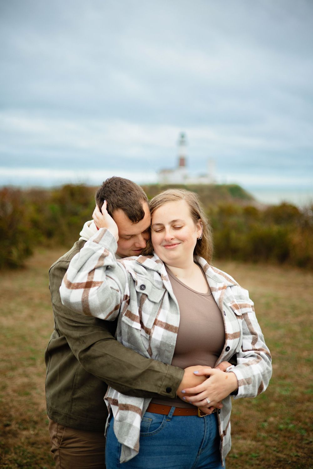 A couple embraces tenderly in an outdoor field during autumn with soft overcast lighting.
