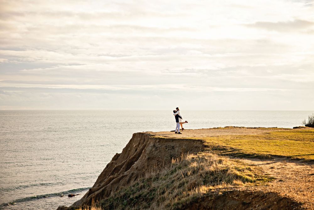 A panoramic view of a rugged coastal cliff edge overlooking a misty ocean during golden hour.