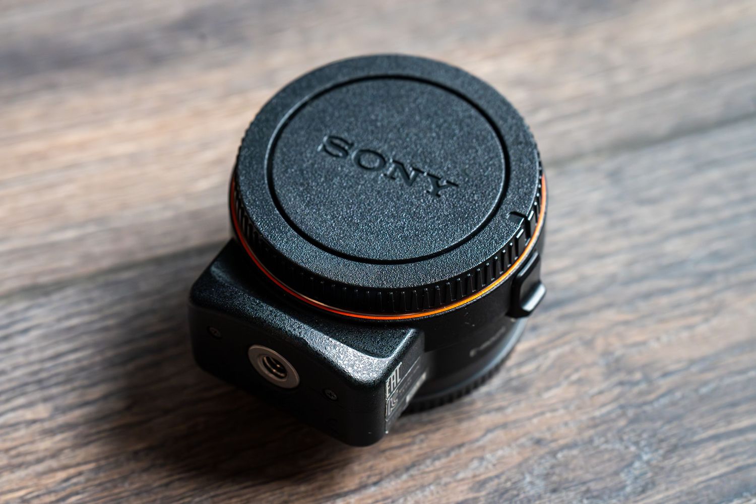 A Sony camera lens cap on a wooden surface shown from multiple angles in a sequence of images.