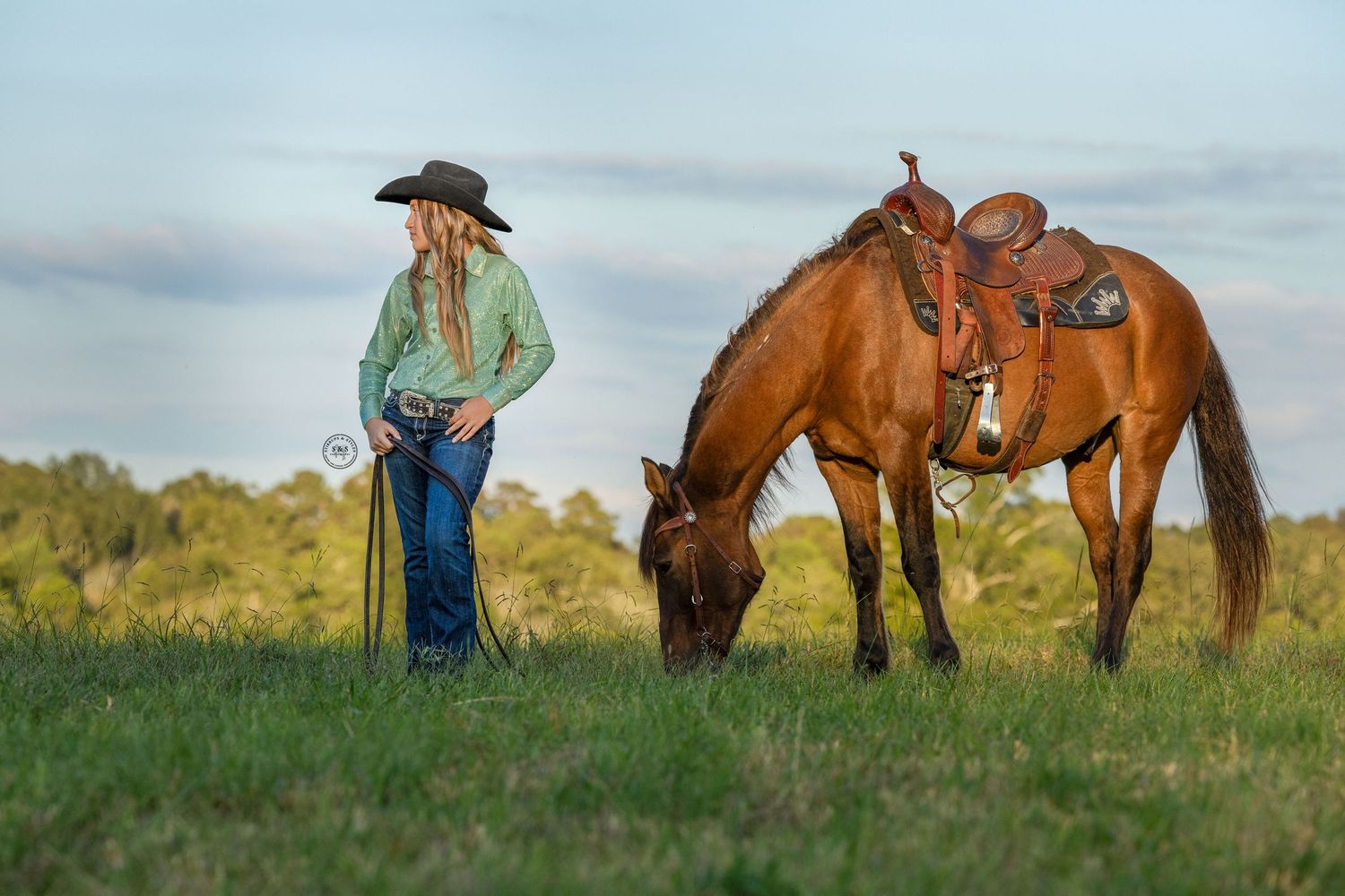 A group of chestnut horses stand in a wooded area while someone in denim interacts with them on a fall day.