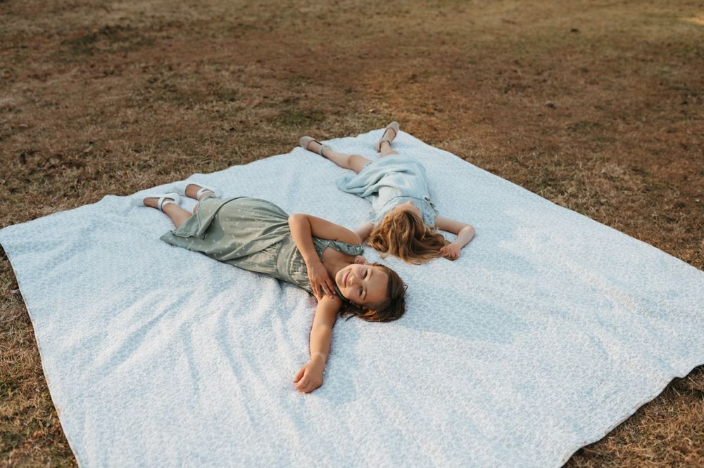 Person lying down on a white blanket in a grassy outdoor setting during a photo session.