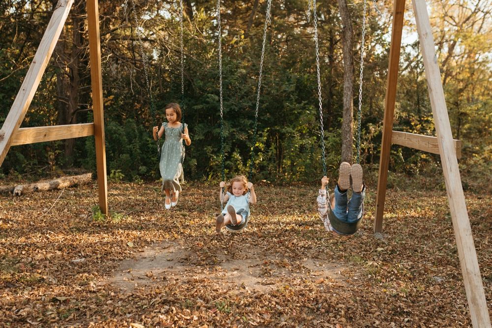 Children playing on wooden swings at sunset in a park with autumn leaves scattered on the ground.