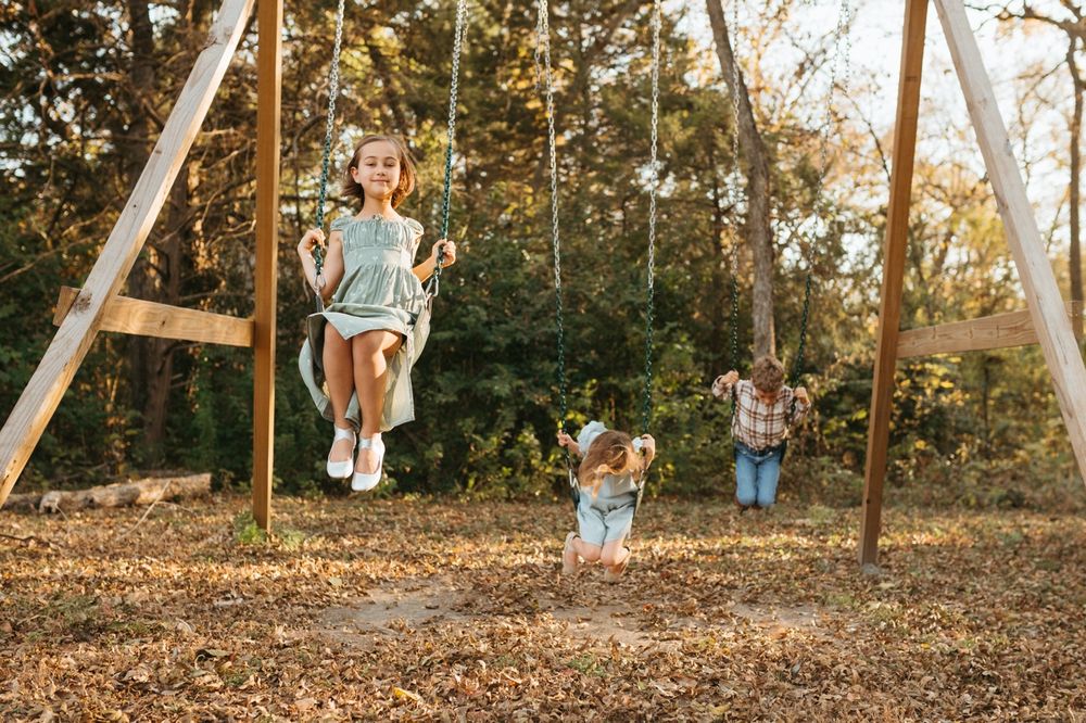 Children playing on wooden swings at a playground on an autumn afternoon in a wooded area.