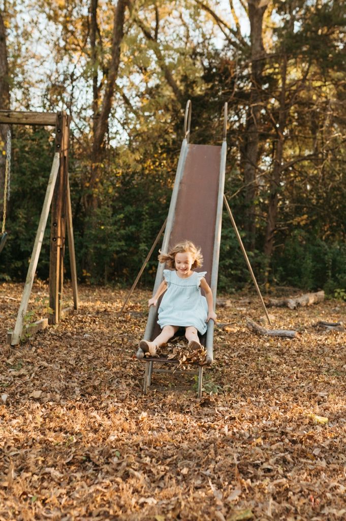 A swing set surrounded by fallen autumn leaves in a backyard setting during golden hour.