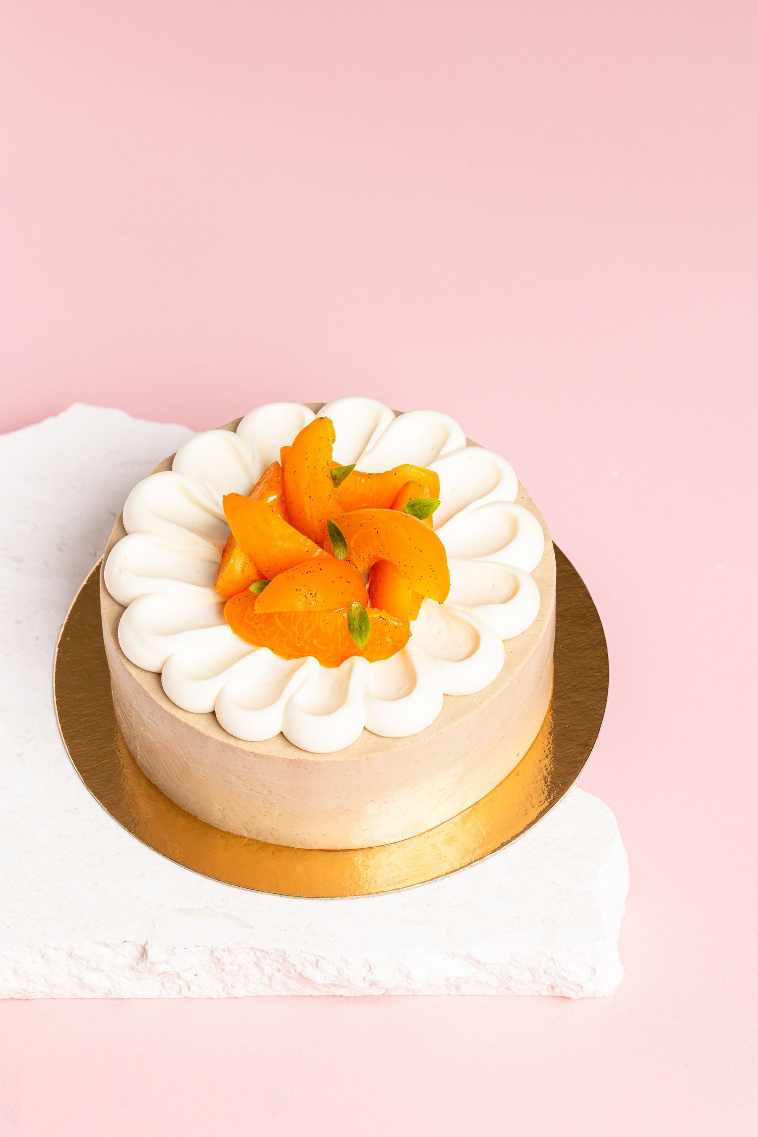 Elegant square pastry with white cream swirls and gold accents on a pink background showcases delicate geometric patterns.