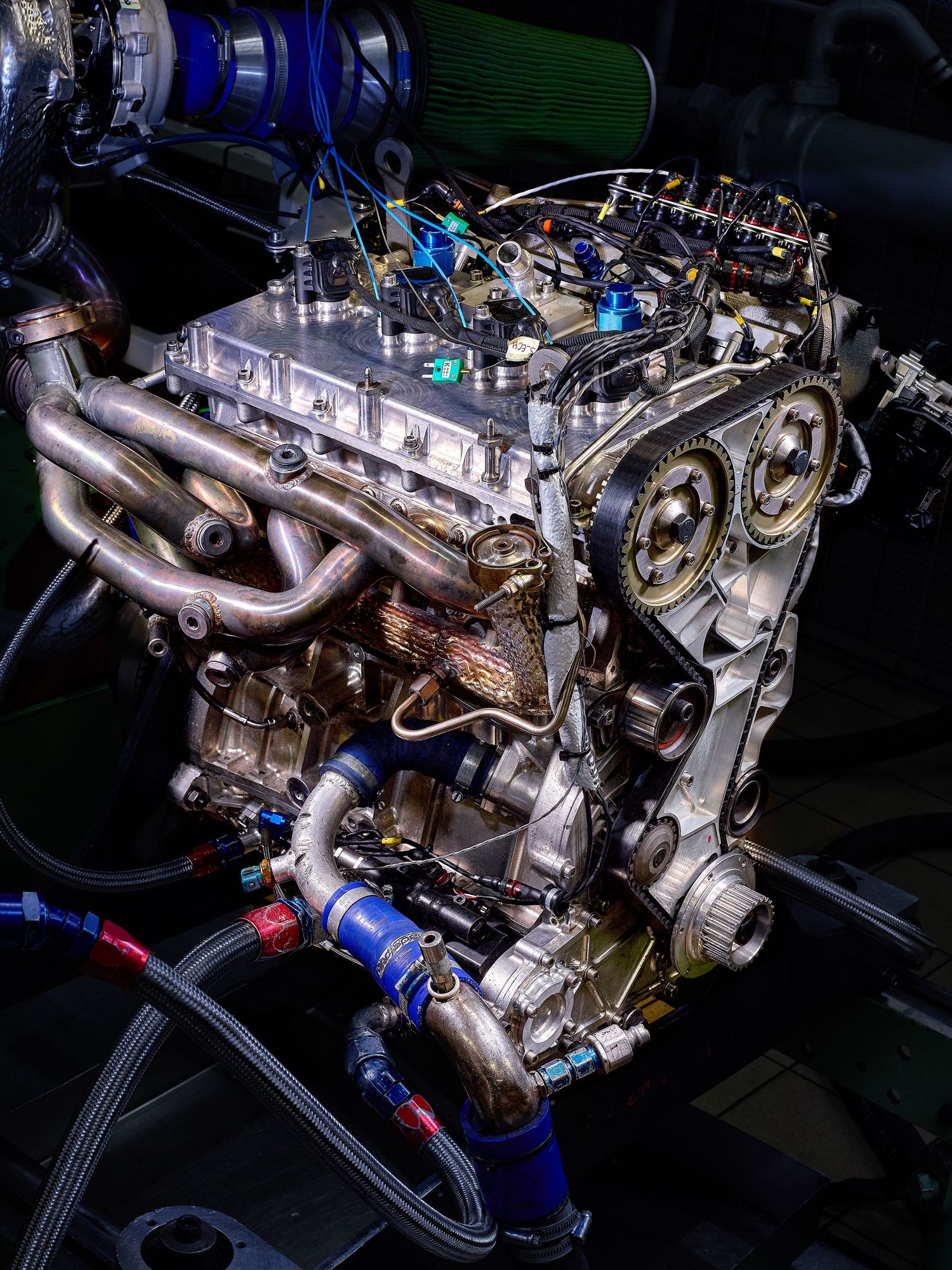 Close-up view of a custom turbo engine setup with silver exhaust manifolds and blue performance components in dark lighting.
