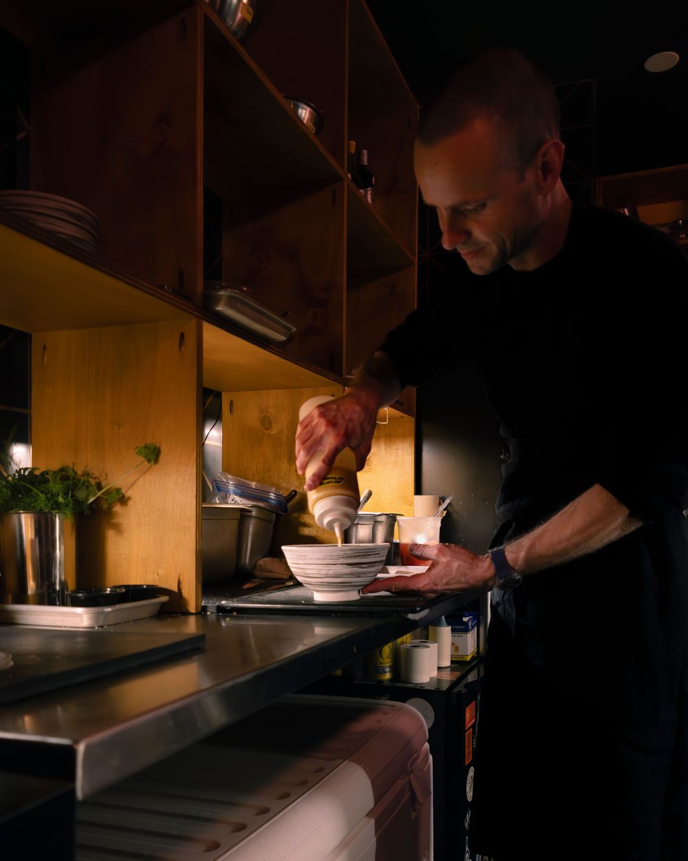 Chef preparing dishes in a dark professional kitchen with focused lighting.