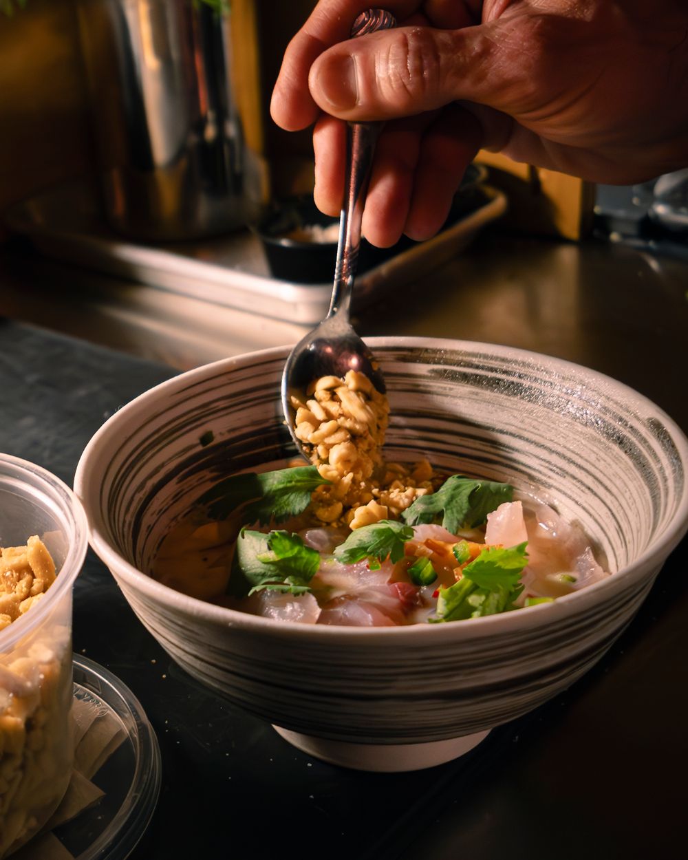 Chef adding final garnishes to an elegantly plated dish in a ceramic bowl.