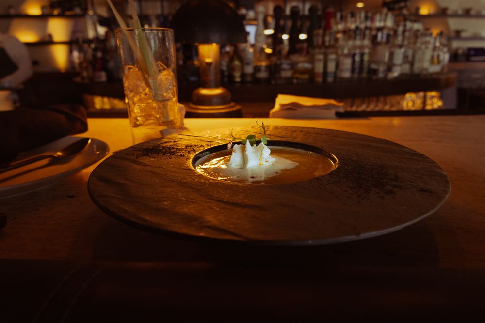 Artfully plated dessert with edible flowers and garnishes in a dimly lit upscale restaurant setting.