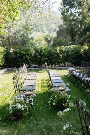 Garden ceremony setup with folding chairs and white flowers lining stone pathway.