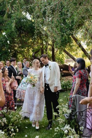 Guests surround a newlywed couple during an outdoor garden wedding ceremony with lush greenery.