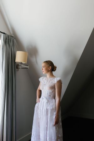 A bridal gown with delicate lace details is showcased in a serene bedroom setting.