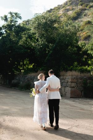 Couple walking along stone wall path in outdoor garden setting.