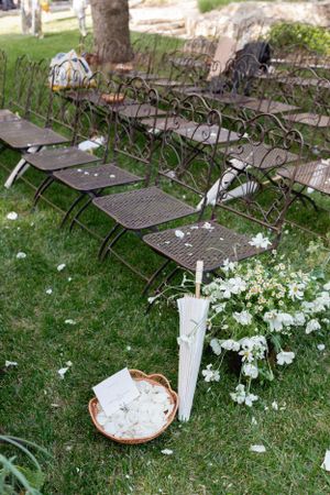 Metal folding chairs arranged on grass with white floral decorations and a vintage umbrella.