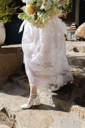 White lace wedding dress hem and vintage-style shoes on stone steps.
