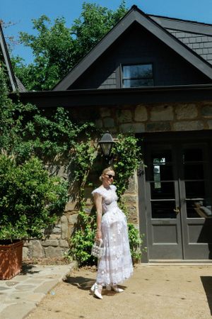 White lace dress against stone building with green foliage.