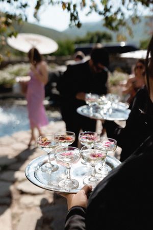 Silver trays of champagne glasses being served at an elegant outdoor event.