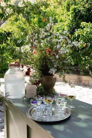 Elegant wedding drinks station with glassware and floral arrangements in a garden setting.