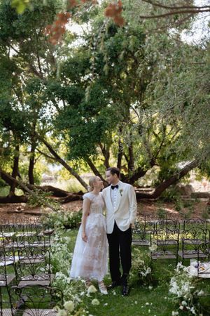 A romantic outdoor wedding ceremony setup with chairs and floral decorations under blooming trees.