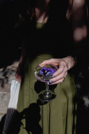 Hand holding an elegant cocktail glass with purple flowers against a dark background.