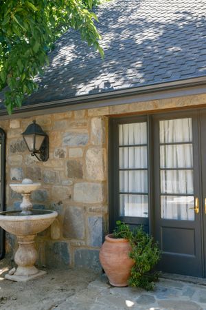 Stone cottage entrance with vintage lantern and decorative fountain against gray shingle roof.