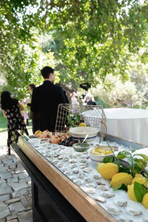 Raw oyster bar display with fresh lemons and garnishes under outdoor canopy.