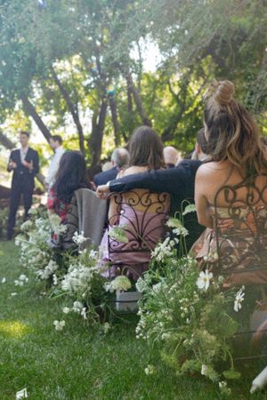 Wedding ceremony guests seated in ornate chairs surrounded by white floral arrangements.