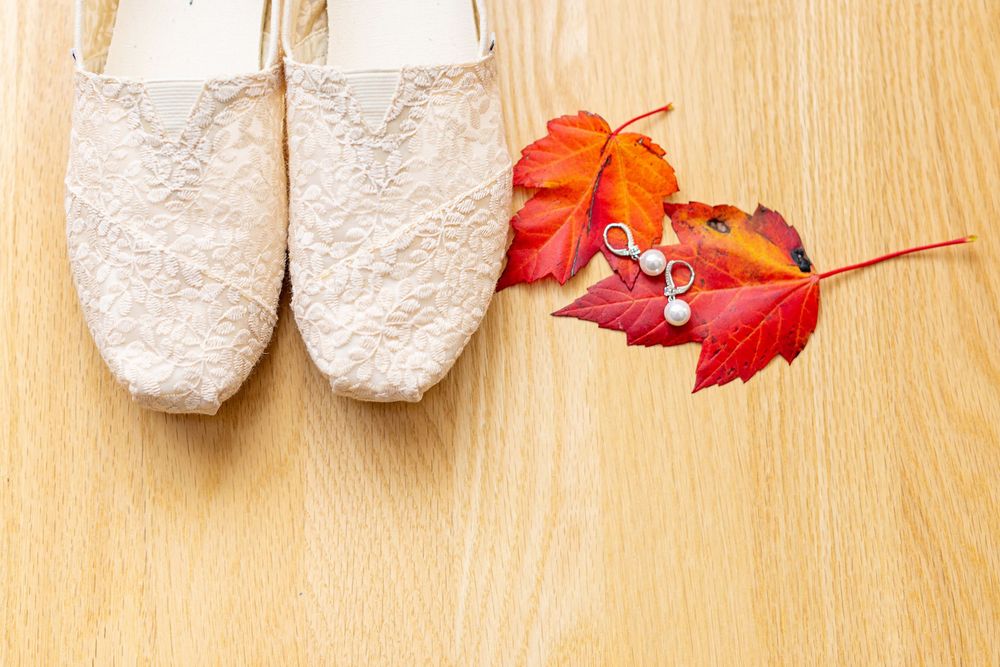 White plush slippers arranged in a row on a light wooden floor with autumn maple leaves as decorative accents.