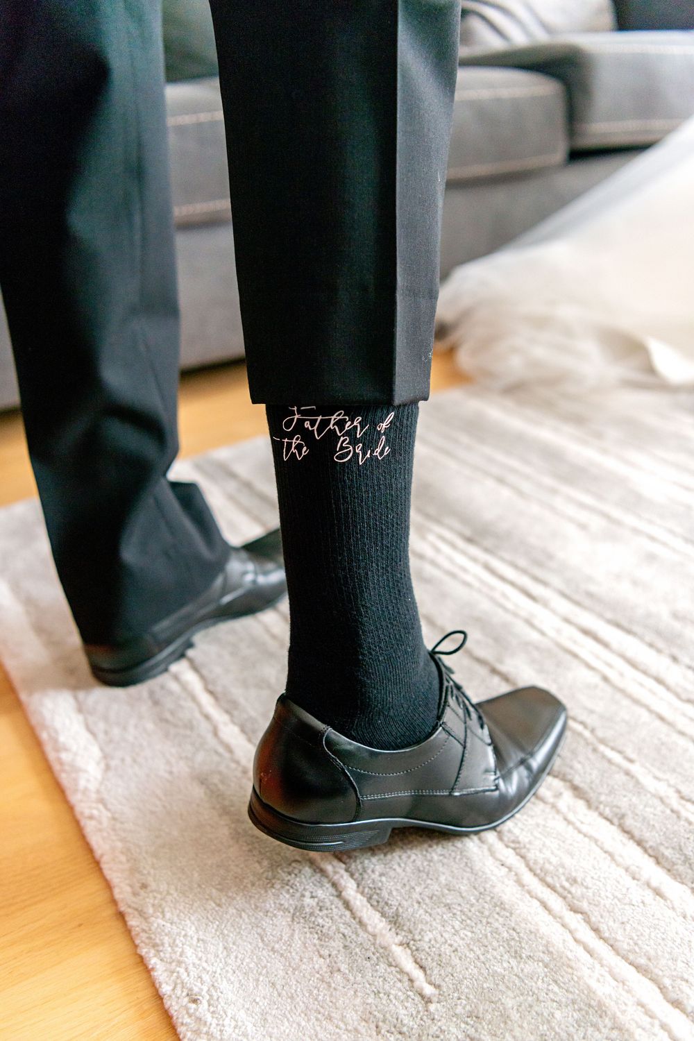 Close-up of black dress sock with 'From 9 to 5' text worn with formal leather oxford shoe on gray carpet.