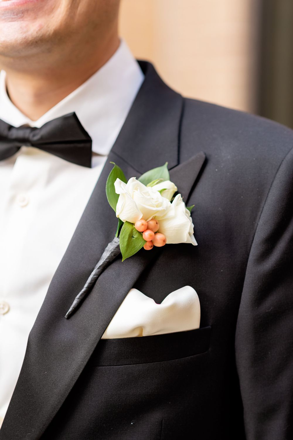 A row of elegant white rose and peach boutonniere flowers pinned to black formal tuxedo lapels.