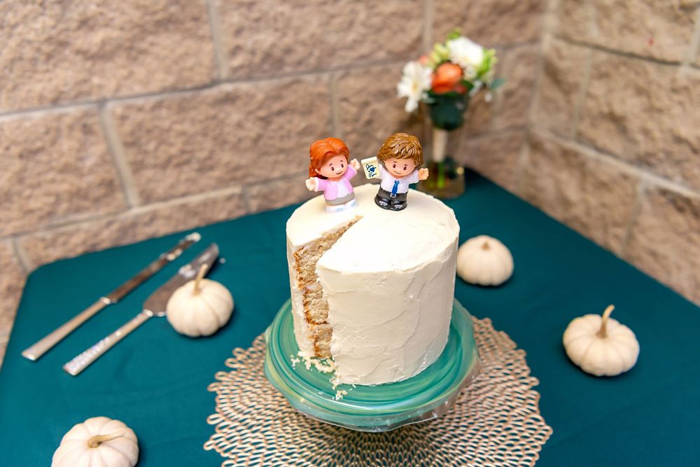 A rustic fall wedding cake decorated with white frosting, small pumpkins, and woodland-themed cake toppers on a teal tablecloth.