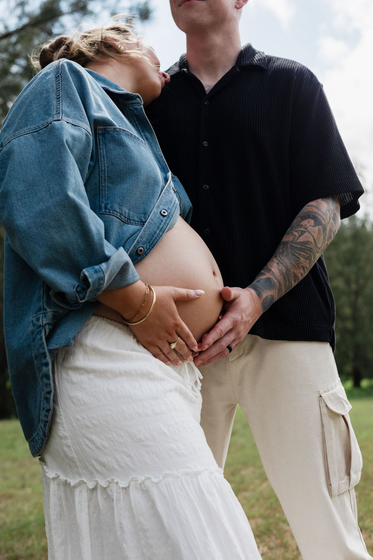 A couple embraces outdoors wearing contrasting black and white outfits with denim, showing affection in a natural setting.