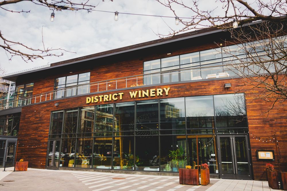 Exterior view of a modern rustic District Winery DC wedding venue with wood paneling and large glass windows along the waterfront.