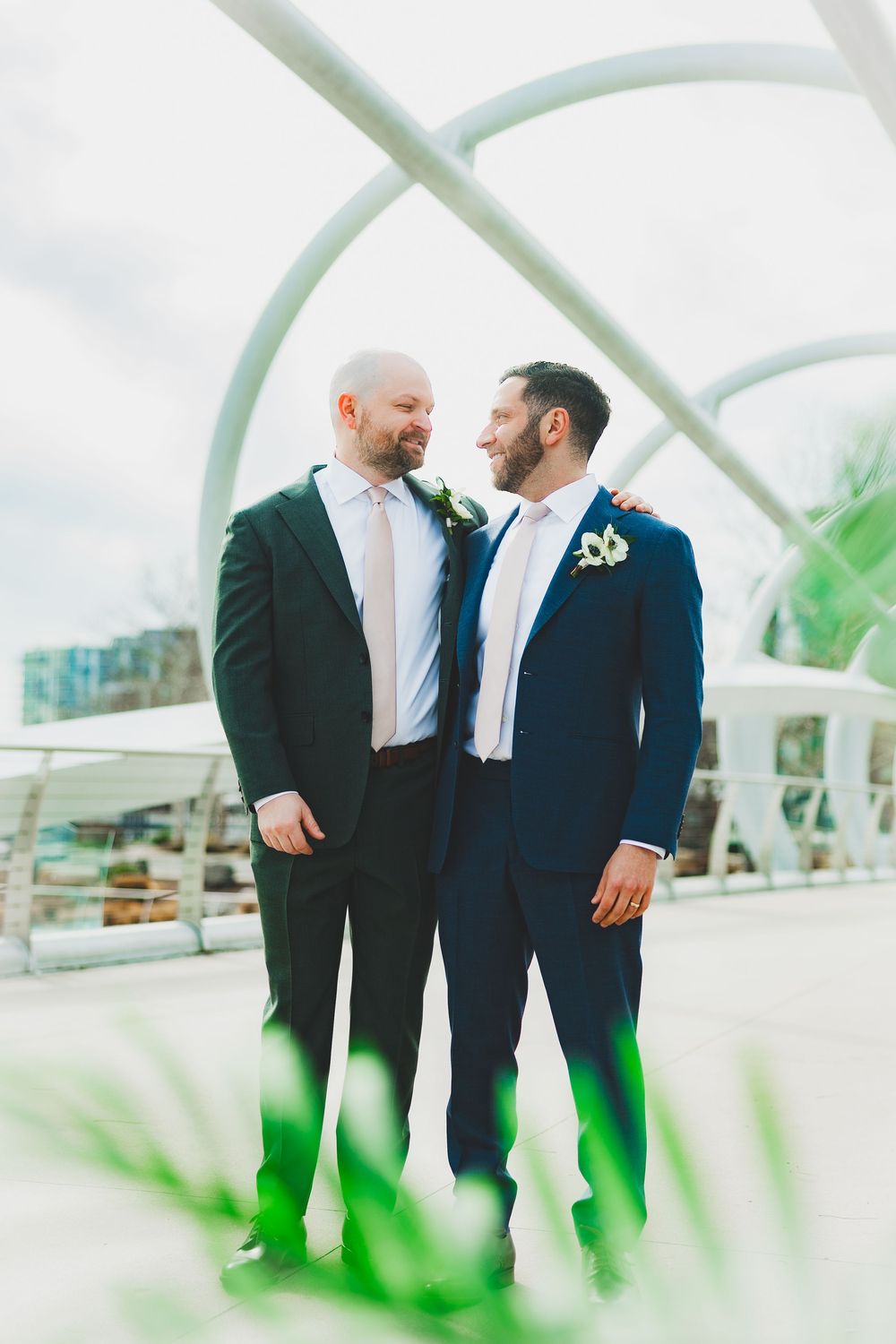 Grooms in formal suits share an intimate moment together in a bright, modern setting on the riverside walkway of the district winery dc