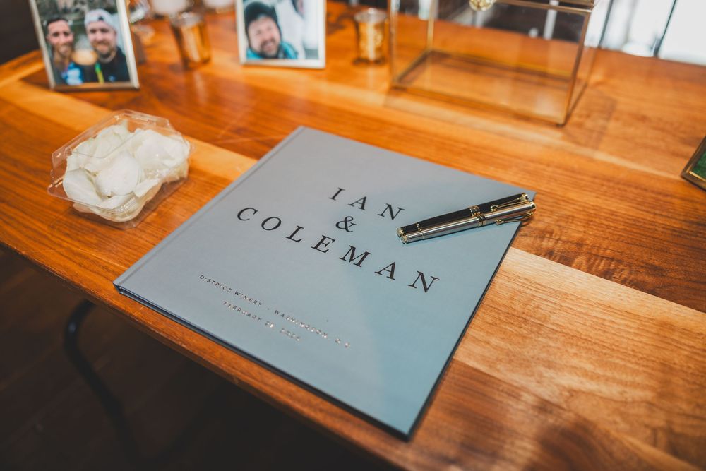 Light blue wedding signing book with stationery arranged on a polished wooden desk surface.