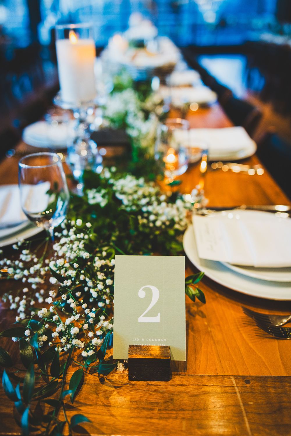 Table number two card sits on rustic wooden dining table with baby's breath flowers and elegant place settings.