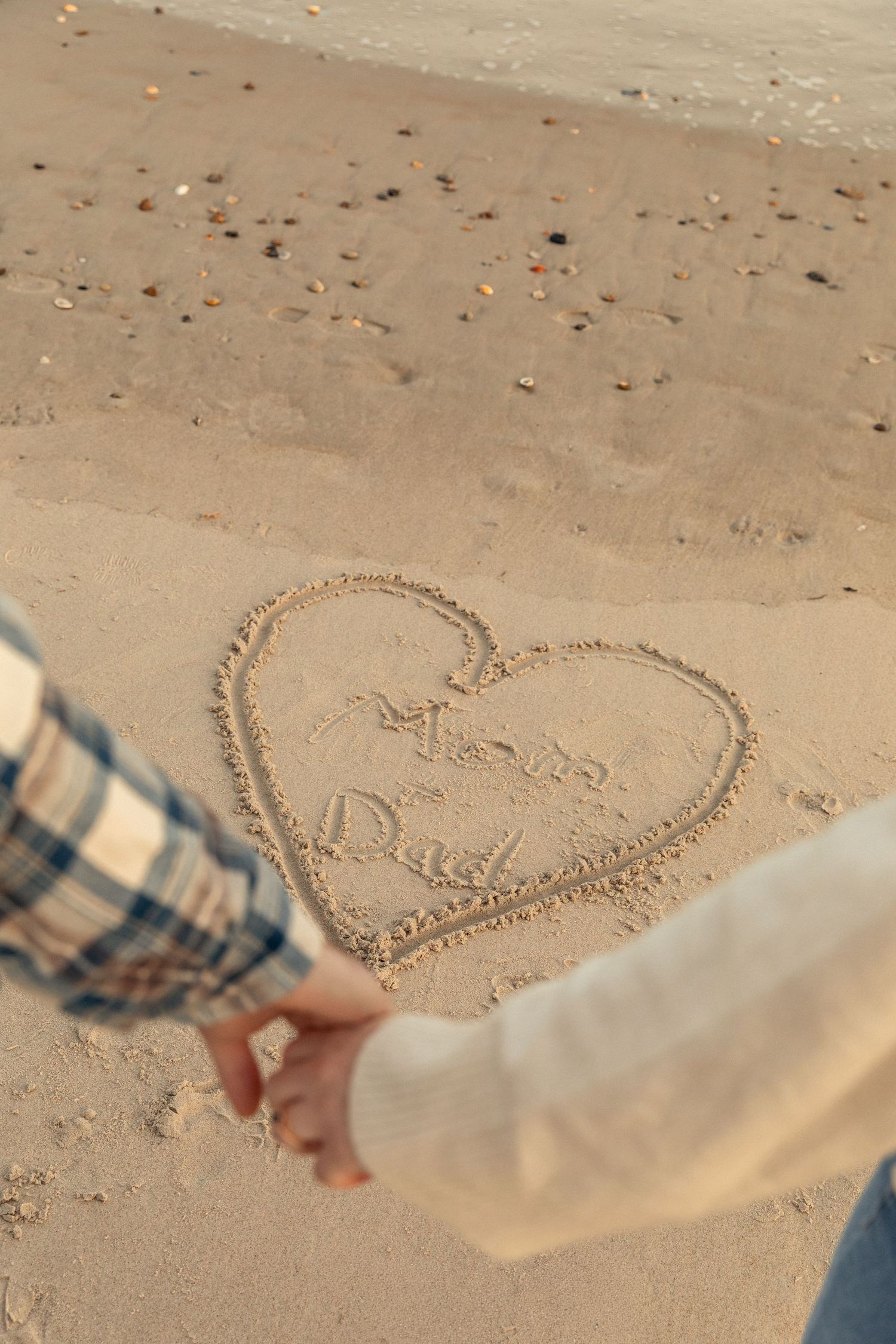 Two people holding hands while looking at a heart drawn in the sand on a beach.