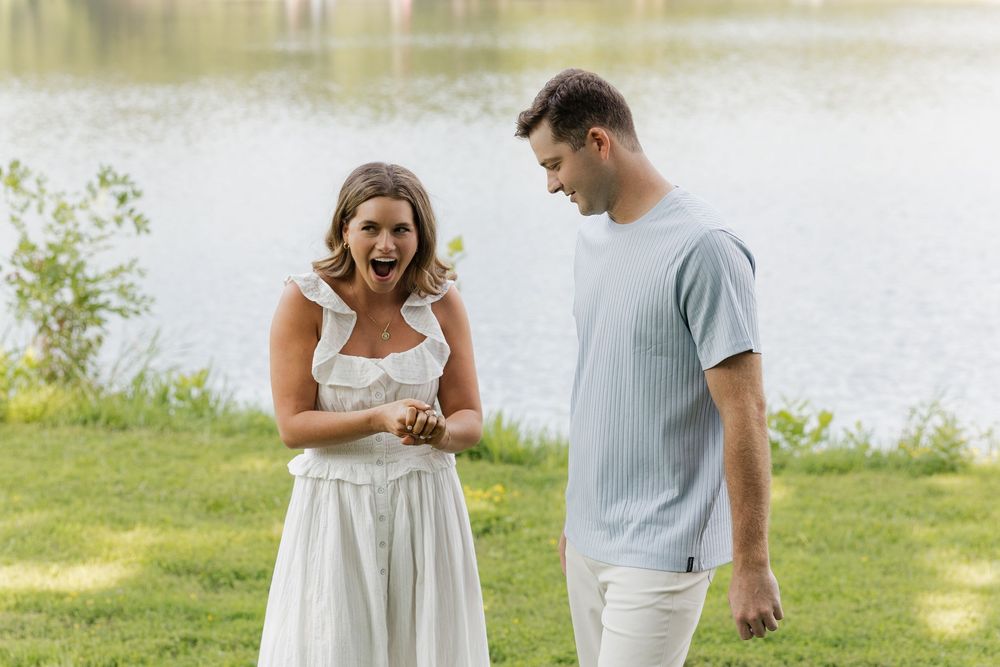 A couple in white and gray attire shares a romantic moment while walking along a lakeside path in summer.