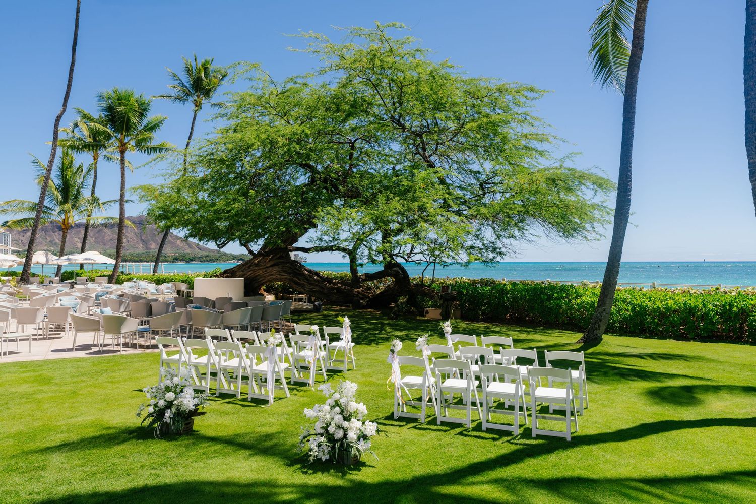 Outdoor beach wedding ceremony setup with white chairs on green lawn, palm trees, and ocean view in Halekulani Hotel.
ハレクラニホテルウェディング