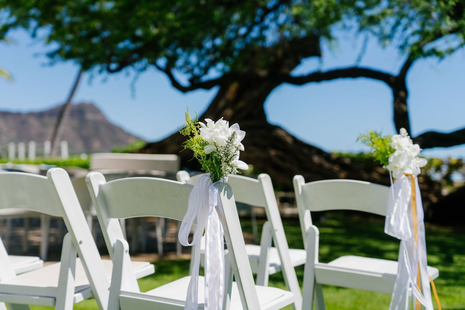 White folding chairs with floral bouquets and ribbon decor set up for an outdoor wedding ceremony in Halekulani Hotel.
ハレクラニホテルウェディング